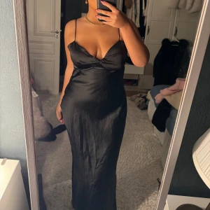 Svart långklänning med smala axelband - Elegant svart långklänning med smala axelband och en figurnära passform. Klänningen är i 42 men passar även 40!