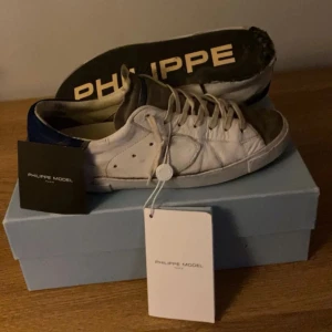 Vita sneakers från Philippe Model - Snygga vita sneakers från Philippe Model med blå detaljer och snörning. Perfekta för en stilren look. Man blir skönazzttt på gädha om man köper🤙🏼😉