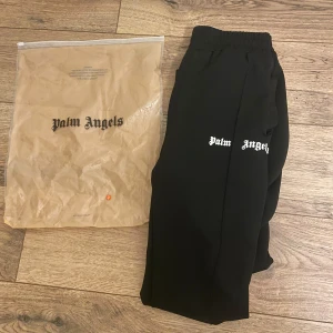 Svarta byxor från Palm Angels - Snygga svarta byxor från Palm Angels med vit text på låret och vita ränder längs sidorna. Byxorna är felfria, oanvända! Priset går inte att DISKUTERAS!