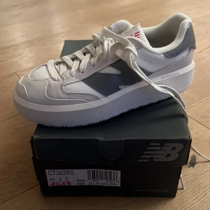 Vita och grå sneakers från New Balance - Snygga och bekväma sneakers från New Balance i vitt och grått. Skorna har en klassisk design med snörning och en robust sula för extra komfort. Perfekta för en stilren vardagslook.