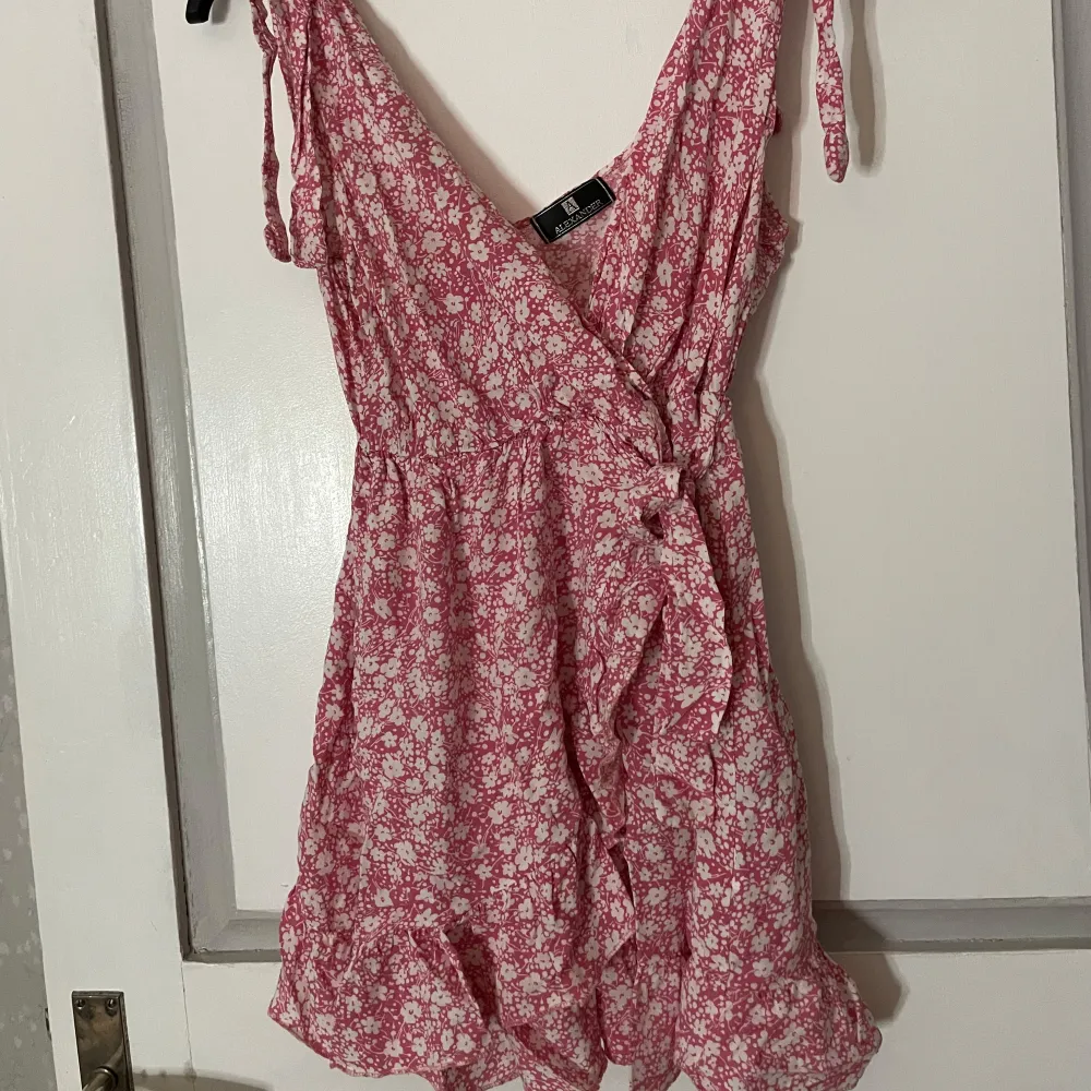 Charmig rosa klänning med blommigt mönster från Alexander. Den har volangdetaljer och knytband vid axlarna. Perfekt för sommarens varma dagar. Köpt i spanien för 500kr och har endast använts 1 gång🤗. Mekot.