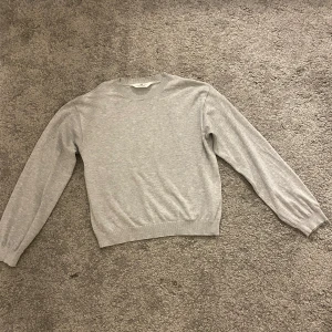 Grå tröja från H&M - Säljer en stilren grå tröja från H&M i storlek 146/152. Tröjan har en klassisk design med långa ärmar och rund halsringning. Perfekt för en avslappnad look.