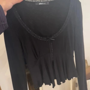 Svart långärmad topp från Gina Tricot - Snygg svart långärmad topp från Gina Tricot med dekorativ knytning framtill. Toppen har en volangdetalj vid nederkanten 