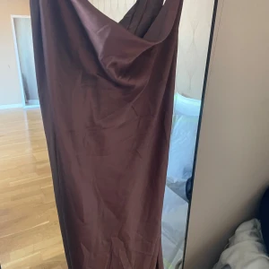 Brun långklänning med öppen rygg - snörning - Elegant brun långklänning med snörning i ryggen. Klänningen har en draperad design och är perfekt för en stilfull look.