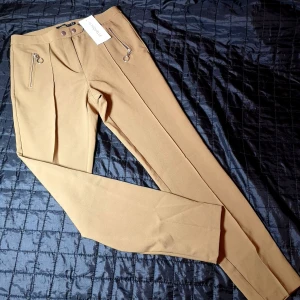 Nya byxor från Chiquelle  - Helt nya och snygga byxor från Chiquelle med prislapp kvar. Byxorna är i stretchmaterial. De är märkta med storlek 40, men de är som en 38 i storleken. Färgen är typ varm brunbeige. 