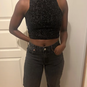 Svart glittrig croppad topp - Snygg svart glittrig croppad topp med blommigt mönster. Perfekt för en utekväll eller fest. Toppen är ärmlös och har en tight passform.