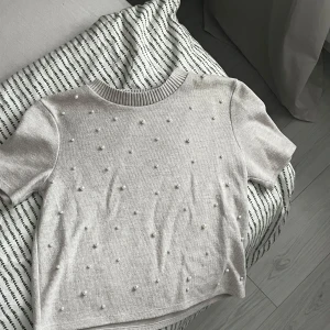 Rosa/vit kortärmad tröja med pärlor - Säljer en stilren rosa/vit tröja med korta ärmar och dekorativa pärlor över hela framsidan. Tröjan har en ribbad rund halsringning och är perfekt för en elegant vardagslook.