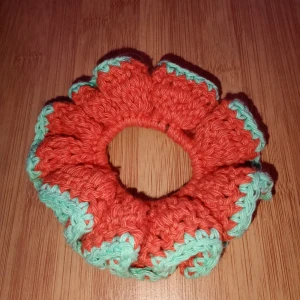 Virkad scrunchie - Snygg och unik virkad scrunchie i orange med gröna detaljer. Perfekt för att ge din frisyr en färgglad touch. Den är elastisk och passar de flesta hårtyper. Perfekt accessoarer för både vardag och fest! Skulle du vilja ha en i en specifik färg är det bara att skriva. Alla accessoarer är gjorda av mig.
