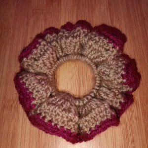 Virkad scrunchie - Snygg och unik virkad scrunchie i beige med lila/plommon lila detaljer. Perfekt för att ge din frisyr en färgglad touch. Den är elastisk och passar de flesta hårtyper. Perfekt accessoarer för både vardag och fest! Skulle du vilja ha en i en specifik färg är det bara att skriva. Alla accessoarer är gjorda av mig.
