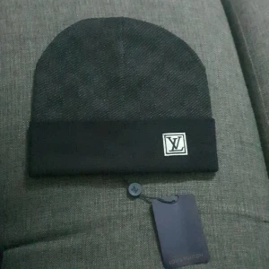 Svart mössa från Louis Vuitton - Snygg svart mössa från Louis Vuitton i nytt skick. Den har en stilren design med ett broderat LV-märke på uppviket. Perfekt för att hålla sig varm och trendig under kyliga dagar. Passar både till vardags och festliga tillfällen.