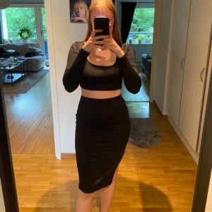 Svart tvådelad klänning - Snygg svart tvådelad klänning med långärmad topp och tight kjol. Kjolen har en slits på sidan som ger en extra touch. Perfekt för fest eller en utekväll. Materialet är stretchigt och bekvämt.