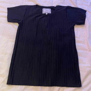 Svart plisserad topp från Skill - Snygg svart topp från Skill i storlek 170. Den har ett plisserat mönster som ger en elegant touch. Perfekt för både vardag och festliga tillfällen. Använd ett fåtal gånger och utan defekter.🖤