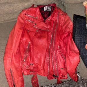 Röd skinnjacka från Jofama by Kenza NYSKICK - Säljer en cool röd skinnjacka från Joe M. Jackan har flera dragkedjor och knappar som ger den en edgy look. Perfekt för höst och vår, och funkar lika bra till fest som till vardags. Den är i bra skick och har en snygg passform. Den sitter åt rätt tight. 