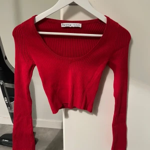 Röd ribbad topp - Säljer en röd ribbad tröja från Bershka. Den är croppad och har långa ärmar med slits ner till. Aldrig använd!