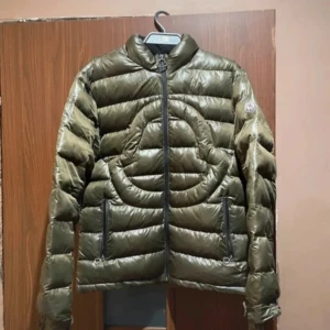 Olivgrön dunjacka från Moncler - Säljer en olivgrön dunjacka från Moncler. Jackan har en snygg quiltad design och dragkedja framtill. Perfekt för höst och vinter. Den är i bra skick men har en liten reva som syns på bilden. Passar perfekt för kyliga dagar! !!!!skriv om ni vill buda!!