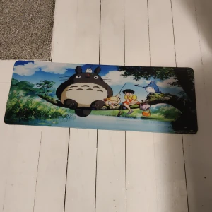 Stor musmatta med Totoro-motiv - Säljer en stor och färgglad musmatta med ett motiv från Totoro. Perfekt för att ge skrivbordet en personlig touch. Mattan har en mjuk yta och en halkfri undersida som håller den på plats. Den är idealisk för både arbete och gaming. 🖱️✨