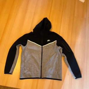 Grå och svart hoodie från Nike - Säljer en snygg grå och svart hoodie från Nike i storlek L. Den har en dragkedja framtill och en huva för extra komfort. Perfekt för höst och vår, med en stilren design och Nike-logga på bröstet. Passar både till träning och vardagsbruk. Den har även en dubbel dragkedja. Pris kan såklart diskuteras.