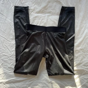 Leggings från Nike - Snygga svarta leggings från Nike med en glittrig finish och det klassiska swoosh-loggan i vitt på benet!