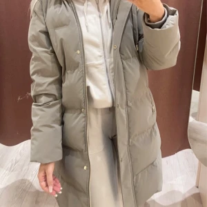 Mossgrön jacka med huva från Zara - xs - Säljer en snygg och varm mossgrön jacka från Zara med huva. Jackan har dragkedja och knappar framtill samt praktiska fickor med dragkedjor i guldiga detaljer. Perfekt för kalla vinterdagar och höstpromenader. Den är i mycket bra skick och passar till både vardag och lite finare tillfällen. Köpt för 899kr och sparsamt använd. 