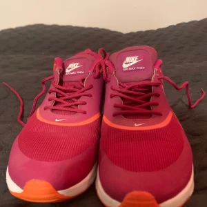 Nike Air Max Thea i vinrött - Säljer ett par snygga Nike Air Max Thea i vinrött. De har en vit sula och den klassiska Nike-loggan på sidan. Skorna är i mycket bra skick och har snörning framtill. Perfekta för både träning och vardag!