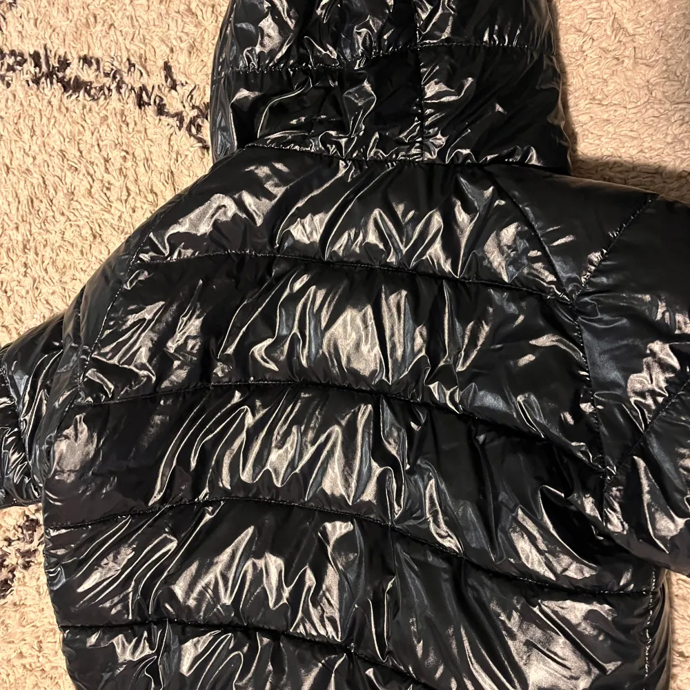 Säljer en snygg svart glansig dunjacka från Moncler. Jackan har en huva och dragkedja framtill, perfekt för kalla vinterdagar. Den är i kaske bra skick och har en stilren design med Moncler-loggan på ärmen. Passar både till vardags och fest! barnens storlek som passar storlek xs. Takit.