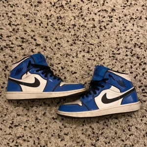 Nike Air Jordans i blått och vitt - Säljer ett par snygga Nike Air Jordans i blått och vitt. Skorna har svarta snören och en klassisk Nike-logga på sidan. Perfekta för både vardag och fest! De är i bra skick med lite slitage på sulan. Passar perfekt för dig som vill ha en stilren och sportig look.