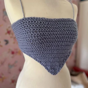 Handgjord virkad topp i lilablått - Säljer en unik handgjord virkad topp i en härlig lilablå nyans. Toppen är ärmlös med smala axelband, perfekt för sommardagar. Den är triangelformad och ger en bohemisk känsla. Passar perfekt till festivaler eller en dag på stranden!