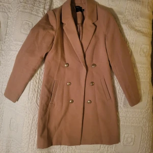 Beige/brun kappa - Säljer en stilren beige/brun kappa i mycket bra skick. Den har en klassisk design med dubbelknäppning och långa ärmar. Perfekt för höst och vår, och funkar lika bra till vardags som till fest. Storlek dam xs.