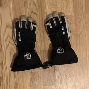 Svarta Hestra handskar - Säljer ett par svarta Hestra handskar bra skick! De har en snygg design med vita detaljer och är perfekta för vintersport. Handskarna har justerbara remmar vid handleden för bättre passform och är gjorda i slitstarkt material. Perfekta för kalla dagar! ❄️