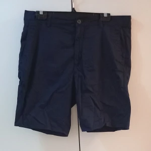 Mörkblå shorts - Säljer ett par mörkblå shorts i bra skick. De har en knapp och dragkedja framtill. Perfekta för sommardagar eller en avslappnad vårutflykt. Passformen är normal och de är gjorda i ett lätt och bekvämt material.