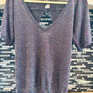 Glittrig topp från Jester - Säljer en superfin glittrig topp från Foster. Den är mörk med ett skimrande glittermönster och har en snygg v-ringning. Toppen har korta ärmar och en söt rosett på baksidan med en öppen ryggdetalj. Perfekt för festliga tillfällen! ✨