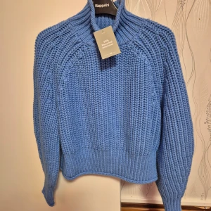 Blå stickad tröja från hm - Säljer en ny och  superfin blå stickad tröja från hm Den är i nytt skick och har en mysig, ribbad design med långa ärmar. Perfekt för höst och vinter när du vill hålla dig varm och stilren. Tröjan har en hög krage som ger extra värme och stil. Passar perfekt till jeans eller kjol!
