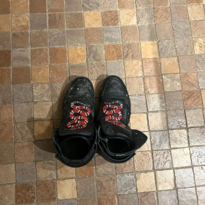 Svarta boots med ormmönster - Säljer ett par svarta boots i skinn med coolt ormmönster i rött och vitt på framsidan. De har en robust design med snörning och är i bra skick, men med lite slitage. Perfekta för höst och vinter, och ger en edgy touch till din outfit!