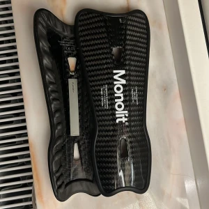 Svart Monolit benskydd - Säljer svarta Monolit benskydd i kolfiber. Perfekt för träning. Kommer i ett praktiskt fodral för enkel förvaring och transport. Nästan aldrig andvända.