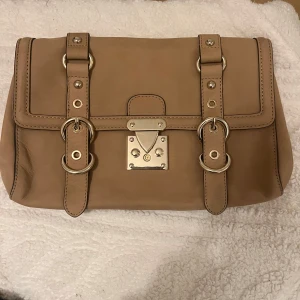 Beige väska från Reiss - Säljer en snygg beige axelväska från Reiss i mycket bra skick. Väskan är gjord av skinn och har en stilren design med guldiga metallspännen. Perfekt för både vardag och fest! 👜✨Lägg gärna prisförslag!