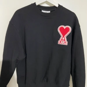 Svart sweatshirt från Ami - "Vill du ha en tröja som både är stilren och bekväm? Kolla in min svarta Ami-tröja med den iögonfallande röda loggan! Perfekt för både vardag och fest. Den avslappnade passformen gör den lätt att matcha med jeans eller chinos. Missa inte chansen att uppgradera din garderob med denna tidlösa klassiker!" 🖤❤️
