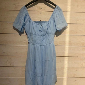 Ljusblå klänning med fickor - Säljer en superfin ljusblå klänning med korta ärmar och knytning framtill. Klänningen är luftig och har fickor och shorts under kjolen.