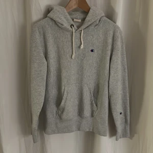 Hoodie Champion - Säljer en grå hoodie från Champion i storlek XS. Den är i mycket bra skick och har det klassiska Champion-loggan broderad på bröstet och ärmen. Perfekt för höst och vinter, med en mysig huva och känguruficka framtill. Skön och stilren för vardagsbruk!