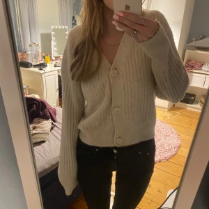 Beige ribbad kofta - Mysig beige kofta med stora knappar framtill. Den är ribbad och har långa ärmar, perfekt för kyliga dagar. Passar både till vardags och lite finare tillfällen. Superbekväm och lätt att matcha med olika outfits!