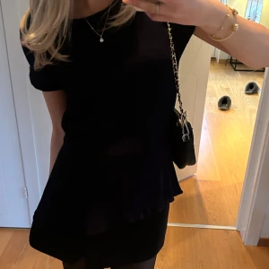 Svart kortklänning med volang - Snygg marinblå blus med volang i nederkant. Perfekt för festliga tillfällen eller till vardags! 