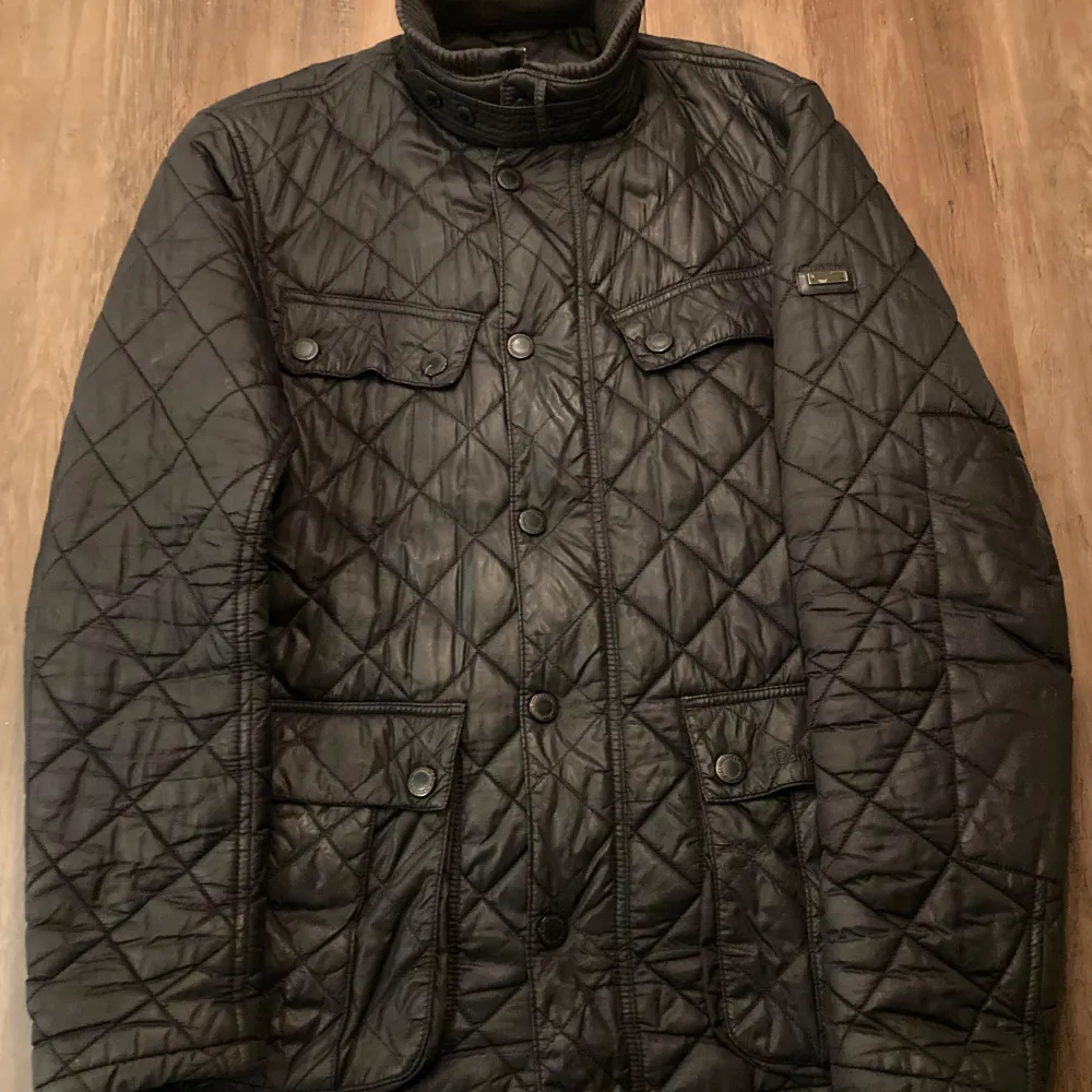 Säljer en snygg svart quiltad jacka från Barbour i storlek M. Jackan har en klassisk design med knappar och två bröstfickor. Perfekt för höst och vår med sitt stilrena utseende och bekväma passform. Den är gjord av polyamid och polyester, vilket gör den både slitstark och lätt att bära.. Jackor.