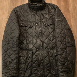 Vinterjacka från Barbour - Säljer en snygg svart quiltad jacka från Barbour i storlek M. Jackan har en klassisk design med knappar och två bröstfickor. Perfekt för vinterjacka, den håller värmen bättre än någon annan jacka jag haft. 