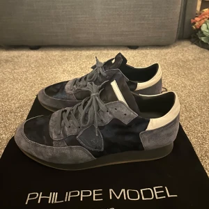 Philippe Model skor trpz  - Säljer ett par Philippe Model sneakers i blå mocka med vita detaljer. Skick 9/10, knappt använda. Köp för endast 1999. Stolrek 44 men passar 43. Dustbag tillkommer. Hör av dig vid frågor eller funderingar!
