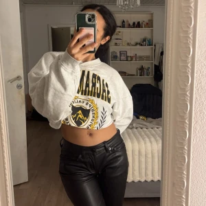 Vit croppad sweatshirt - Säljer en supercool vit croppad sweatshirt med tryck i svart och gult. Perfekt för en avslappnad stil och passar bra till både jeans och kjol. Den har en loose passform och långa ärmar, vilket gör den bekväm och trendig. Perfekt för höst och vår!