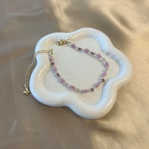 Sött handgjord armband med rosa blommor - Detta armband är supergulligt med små rosa blommor och glittriga detaljer. Perfekt för att ge en romantisk touch till din outfit. Armbandet har en justerbar kedja i guldton för perfekt passform. Passar både till vardag och fest! Kedjan är 14k guld pläterad stålfritt stål. 