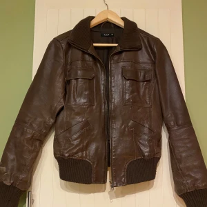 Brun skinnjacka från Vila - Säljer en snygg brun skinnjacka från Vila i storlek M. Jackan har en dragkedja framtill och ribbade muddar vid ärmslut och nederkant. Perfekt för höst och vår med sin stilrena design och bekväma passform.