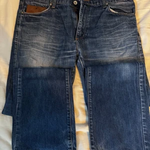 Blå jeans med fickdetaljer - Snygga blå jeans med en klassisk femficksdesign och knappar på bakfickorna. De har en lätt tvättad look och en läderdetalj vid midjan. Perfekta för en avslappnad stil.