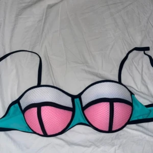Färgglad Bikinitopp  - Snygg Bikinitopp i en mix av turkos, rosa och vit med svarta detaljer. Den har en unik design med vadderade kupor och justerbara axelband för bästa passform. Är i storlek L men hade funkat för S och M också. Kontakta mig vid mer information! 