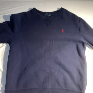Mörkblå tröja från Polo Ralph Lauren - Säljer en stilren mörkblå tröja från Polo Ralph Lauren med det klassiska röda logotypbroderiet på bröstet. Tröjan har långa ärmar och en rund halsringning. Perfekt för en avslappnad och snygg look. Storlek xl 18-20 är 180cm och den är lite för kort på mig men borde funka för dem som är 170-175 cm 