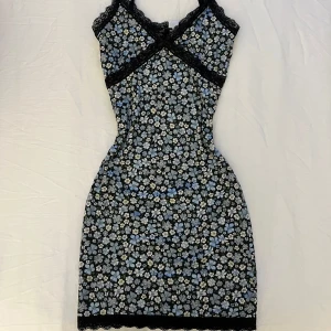 Blommig klänning med spetsdetaljer - Supersöt blommig klänning med svarta spetsdetaljer och smala axelband🌸 Klänningen har en tight passform och är perfekt för varma dagar. Passar på de som har XXS och XS!☺️ Använd ett fåtal gånger och i väldigt bra skick. Säljes pga att den inte kommer till användning. 